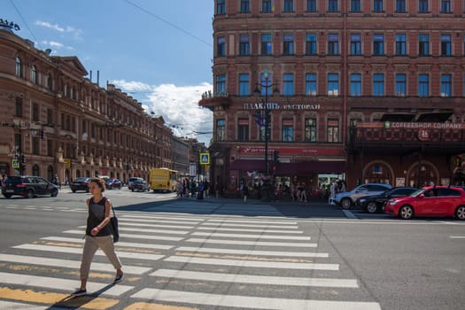 young adult Caucasian woman with black shoulder bag and back jerkin crossing street at sunny day in Saint-Petersburg, Russia: July 25, 2015