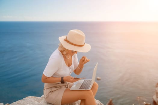 Freelance women sea working on the computer. Good looking middle aged woman typing on a laptop keyboard outdoors with a beautiful sea view. The concept of remote work