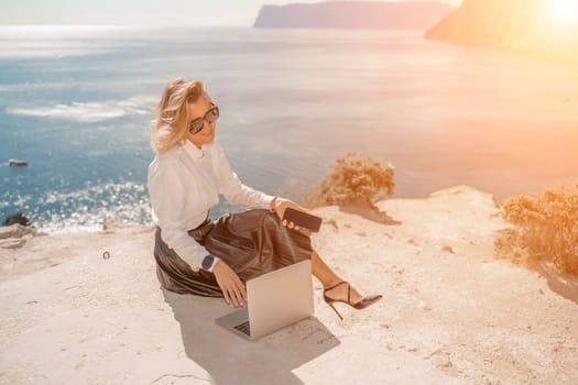 Freelance women sea. She is working on the computer. Good looking middle aged woman typing on a laptop keyboard outdoors with a beautiful sea view. The concept of remote work