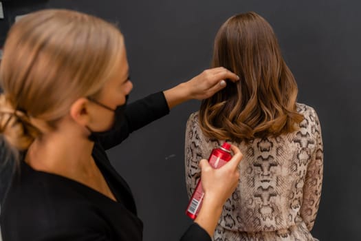 Women salon hairstyle. Hairdresser uses hairspray on client's hair in salon, Portrait of two beautiful women.