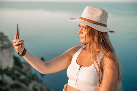 Selfie woman in hat, white tank top and shorts makes selfie shot mobile phone post photo social network outdoors on sea background beach people vacation lifestyle travel concept