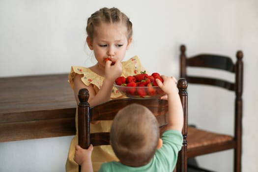 Two young girls eating strawberries in living room smiling