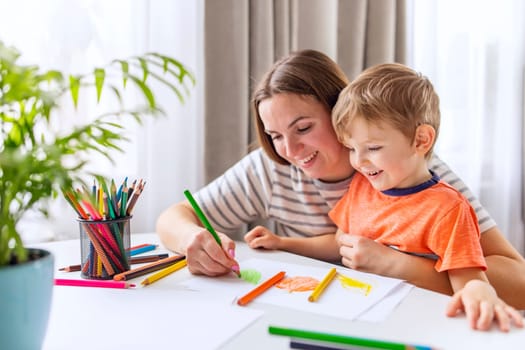 A smiling woman and young boy drawing with colorful pencils at home