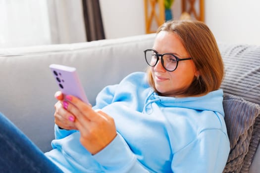 Smiling woman in glasses lounging on sofa with mobile phone