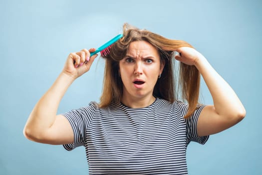 Frustrated young woman with a surprised expression trying to comb through tangled hair, holding a hairbrush.