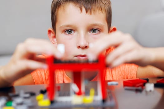Close-up of a young boy deeply focused while assembling a red toy building set, showcasing his concentration and dexterity.