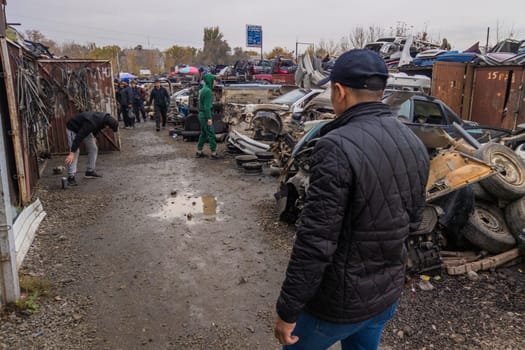 man looking for car parts at open air junkyard and used spare parts market in Kudaybergen, Bishkek, Kyrgyzstan - October 10, 2022