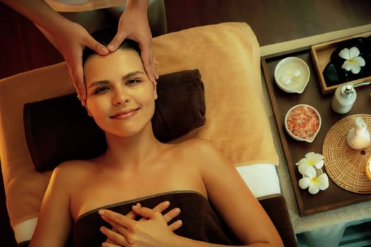 Caucasian woman enjoying relaxing anti-stress head massage and pampering facial beauty skin recreation leisure in warm candle lighting ambient salon spa in luxury resort or hotel. Quiescent