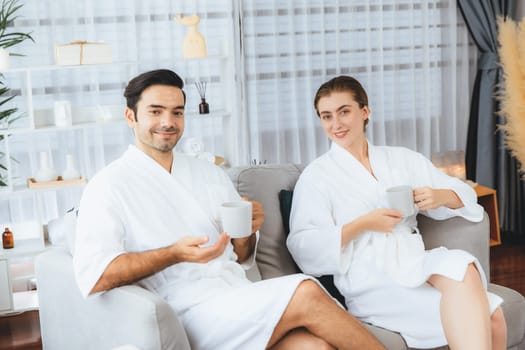 Beauty or body treatment spa salon vacation lifestyle concept with couple wearing bathrobe relaxing with drinks in luxurious hotel spa or resort room. Vacation and leisure relaxation. Quiescent