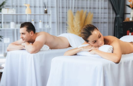 Caucasian couple customer enjoying relaxing anti-stress spa massage and pampering with beauty skin recreation leisure in day light ambient salon spa at luxury resort or hotel. Quiescent