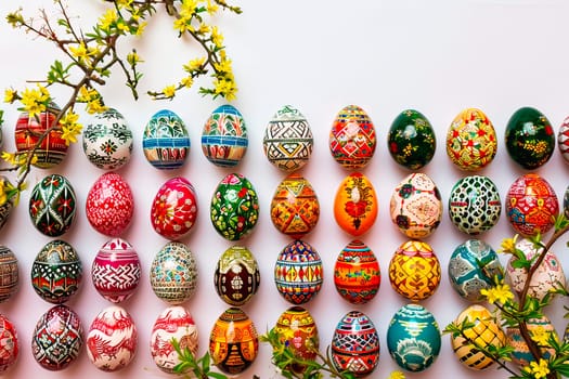 An aerial view of the Easter eggs arranged on a white tabletop. Each Easter egg has a different and unique design. They are hand-painted. The eggs lie equidistant from each other.