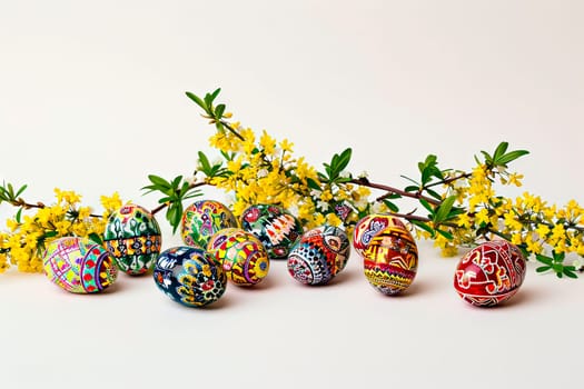 Patterned mottled Easter eggs lie on a white ground next to a branch from a forsythia bush. Easter commemorative artwork on a white background.