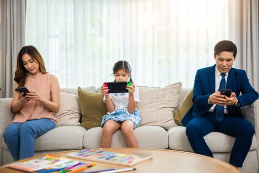 Family don't care about each other. Asian parents ignore their child and looking at their mobile phone at home, gadgets dependence overuse internet social media addiction on sofa living room