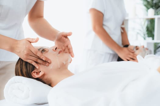Serene modern daylight ambiance of spa salon, couple customer indulges in rejuvenating with facial skincare mask. Facial skin treatment and beauty cosmetology procedure for face. Quiescent