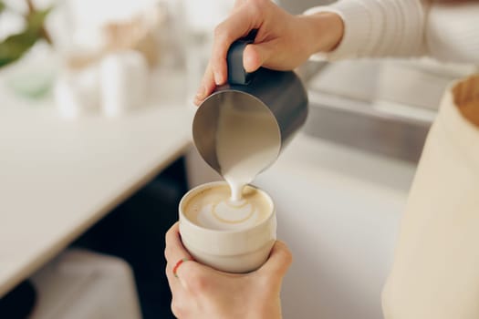 Close up of woman barista in apron pouring hot milk foam into coffee