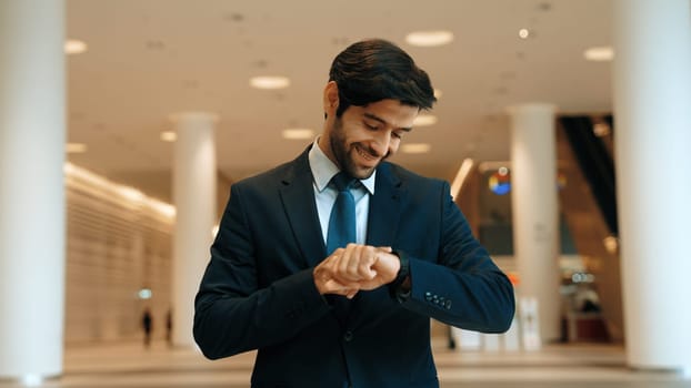 Caucasian smart business man looking at watch while waiting colleague. Executive manager wearing suit while standing at mall with blurred background. Investor wear blue suit check time. Exultant.