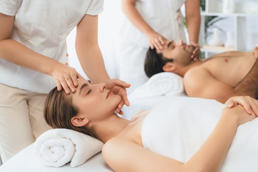 Caucasian couple enjoying relaxing anti-stress head massage and pampering facial beauty skin recreation leisure in dayspa modern light ambient at luxury resort or hotel spa salon. Quiescent