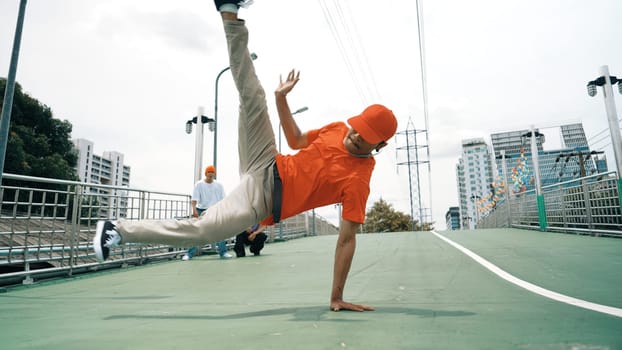 Young happy hipster perform break dancing or foot step with friend moving to hiphop music together. Skilled dancer doing freeze pose and waving hand. Modern lifestyle. Outdoor music 2024. Sprightly.