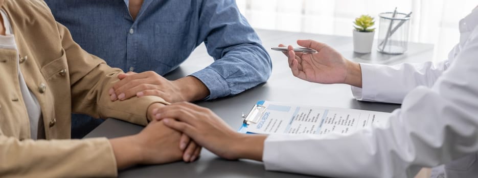 Doctor providing compassionate healthcare consultation while young couple patient holding hand, comfort each other after infertile report. Reproductive and medical fertility consulting. Neoteric