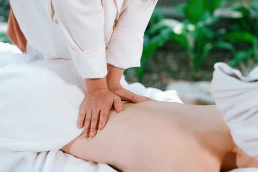 A pretty girl with beautiful skin with white towel receives back massage from Thai professional masseur surrounded by relaxing and peaceful spa environment. Closeup. Focus on back.Tranquility.