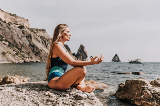 Yoga on the beach. A happy woman meditating in a yoga pose on the beach, surrounded by the ocean and rock mountains, promoting a healthy lifestyle outdoors in nature, and inspiring fitness concept