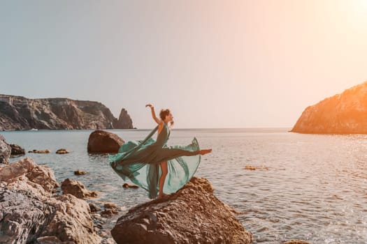 Woman green dress sea. Woman in a long mint dress posing on a beach with rocks on sunny day. Girl on the nature on blue sky background