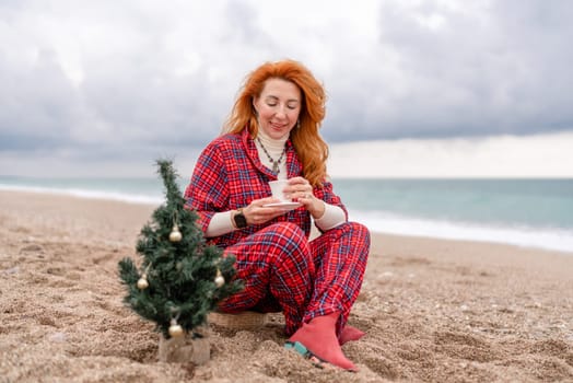 Sea Lady in plaid shirt with a mug in her hands enjoys beach with Christmas tree. Coastal area. Christmas, New Year holidays concep.