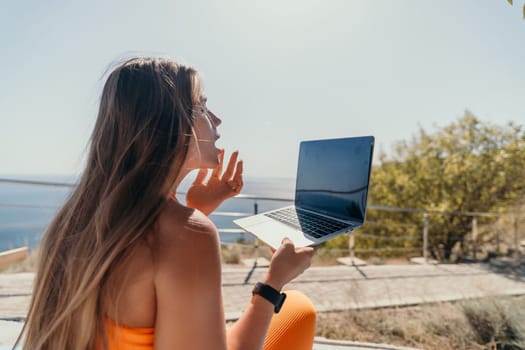 Digital nomad, Business woman working on laptop by the sea. Pretty lady typing on computer by the sea at sunset, makes a business transaction online from a distance. Freelance, remote work on vacation