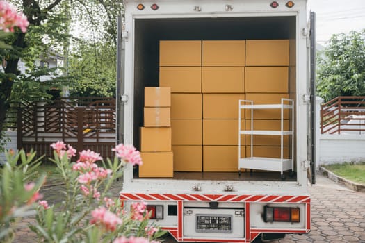 Outdoors a white delivery van and open car trunk carrying moving cardboard boxes. Logistic service for house relocation. Transporting items in crowded truck. Moving Day Concept.