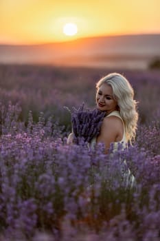 Blonde woman poses in lavender field at sunset. Happy woman in white dress holds lavender bouquet. Aromatherapy concept, lavender oil, photo session in lavender.