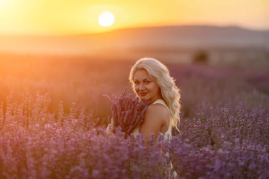 Blonde woman poses in lavender field at sunset. Happy woman in white dress holds lavender bouquet. Aromatherapy concept, lavender oil, photo session in lavender.