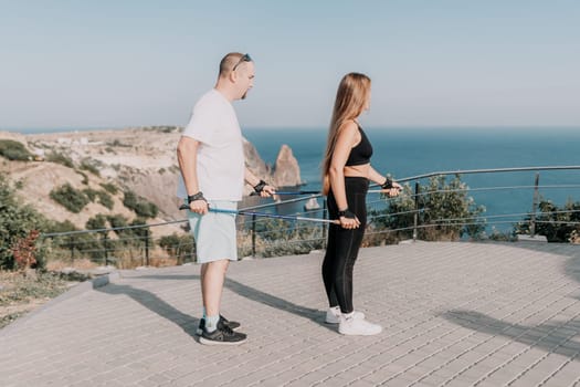 Happy Middle aged couple or friends practicing nordic walking in park near sea. Mature couple with trekking poles walking, practicing Nordic walking outdoors. Aging youthfully and sport concept.