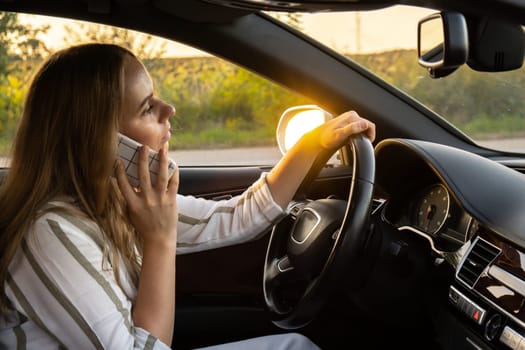 Young woman using mobile phone while driving car on highway road during sunset. Womandriver has accident calling with smartphone for help. Business woman busy driving concept