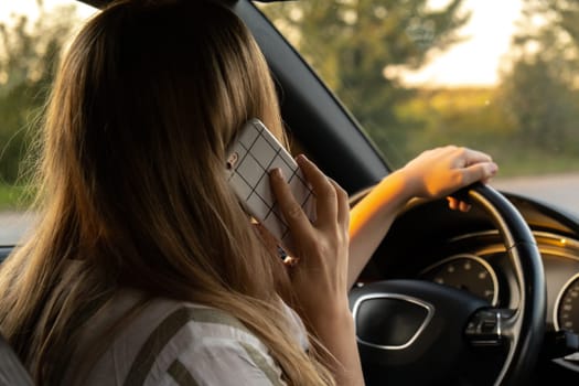 Young woman using mobile phone while driving car on highway road during sunset. Womandriver has accident calling with smartphone for help. Business woman busy driving concept