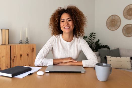Happy young female entrepreneur at home office. Multiracial hispanic woman looking at camera sitting at desk.Working at home concept.
