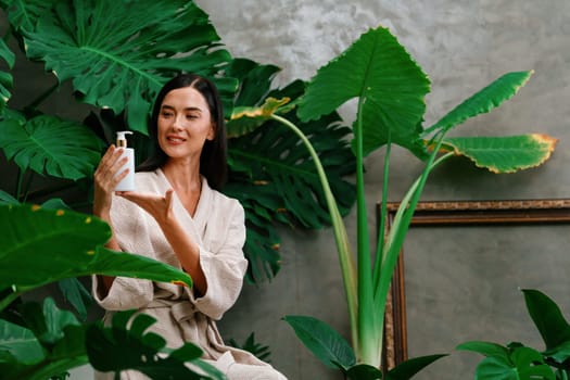 Tropical and exotic spa garden with bathtub in modern hotel or resort with woman in bathrobe holding beauty skincare product while enjoying leisure lush with greenery foliage background. Blithe