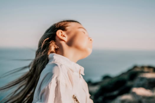 Brown-haired young romantic teenager girl corrects long hair on beach at summer evening wind