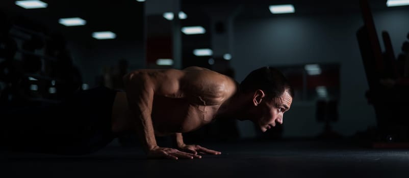 Muscular shirtless man doing push ups in the gym