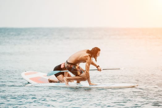 Sea woman and man on sup. Silhouette of happy young woman and man, surfing on SUP board, confident paddling through water surface. Idyllic sunset. Active lifestyle at sea or river