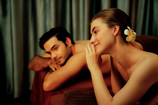 Caucasian couple customer enjoying relaxing anti-stress spa massage and pampering with beauty skin recreation leisure in warm candle lighting ambient salon spa at luxury resort or hotel. Quiescent