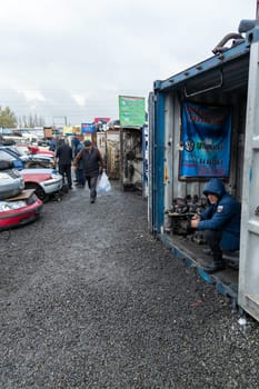 man selling Volkswagen car parts at open air used spare parts market in Kudaybergen, Bishkek, Kyrgyzstan - November 9, 2022