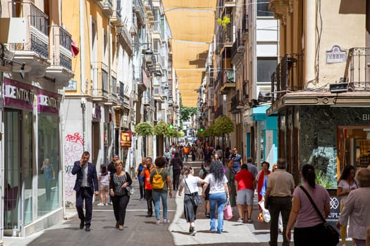 Granada, Spain - May 27, 2019: People walking in a charming narrow shopping street in the historic city centre.