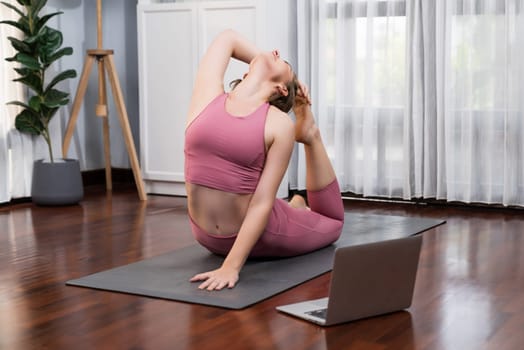 Flexible and dexterity woman in sportswear doing yoga position in meditation posture on exercising mat at home. Healthy gaiety home yoga online training session with peaceful mind and serenity.