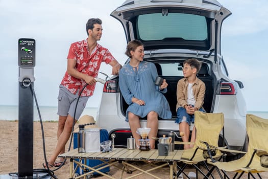 Family vacation trip traveling by the beach with electric car, happy family recharge EV car, enjoying outdoor camping coffee. Seascape travel and eco-friendly car for clean environment. Perpetual