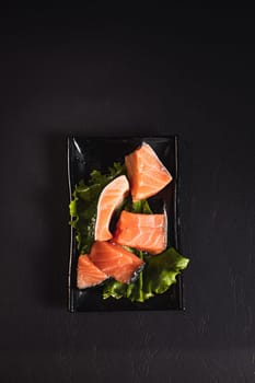 red fish on lettuce leaves on a black plate