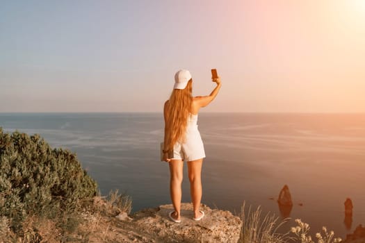 Selfie woman sea. The picture depicts a woman in a cap and tank top, taking a selfie shot with her mobile phone, showcasing her happy and carefree vacation mood against the beautiful sea backgroun.