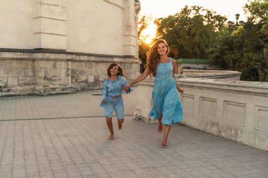 Mother aughter sunset. in blue dresses with flowing long hair against the backdrop of sunset. The woman hugs and presses the girl to her