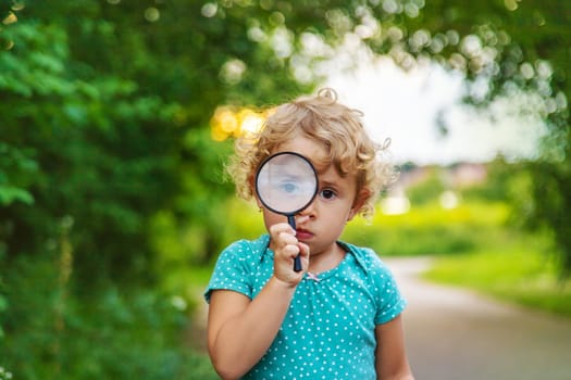 A child looks through a magnifying glass in nature. Selective focus. Kid.