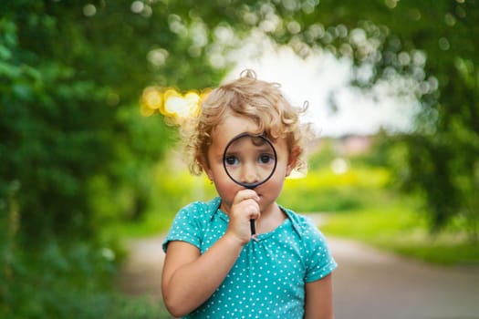 A child looks through a magnifying glass in nature. Selective focus. Kid.