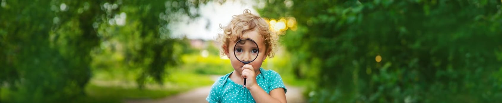 A child looks through a magnifying glass in nature. Selective focus. Kid.